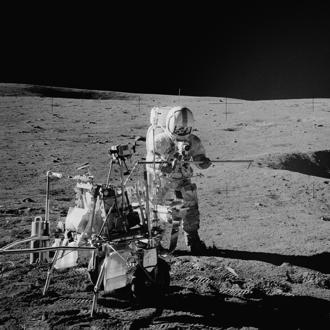 Apollo 14 commander Alan Shepard stands next to the Modularized Equipment Transport (MET), a 2-wheeled handcart, while he assembles a core tube (long narrow pole).